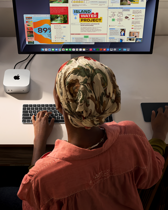 Eine Person tippt an einem Schreibtisch mit einem Mac mini, Studio Display angeschlossen, Magic Keyboard, Magic Trackpad, verschiedene Objekte