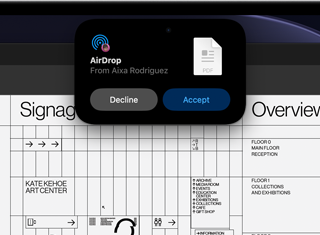 Das Display zeigt die Dynamic Island mit einer AirDrop Anfrage in einem kleinen Fenster über einer geöffneten Adobe Acrobat Datei