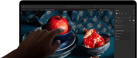 MacBook Pro mit PROLED XDR Display mit einem Stillleben mit Granatäpfeln, blauer Keramik und Textilien, eine Hand reicht nach dem Bildschirm, um mit dem Bild zu interagieren