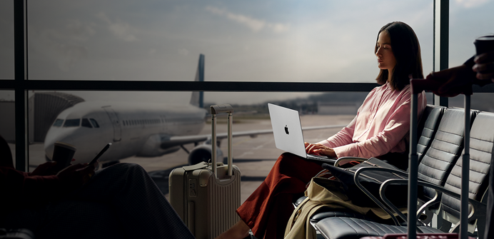 Eine Mitarbeiterin tippt auf einem 14 Zoll MacBook Pro in Silber, das nicht an den Strom angeschlossen ist, während sie am Gate auf ihren Flug wartet